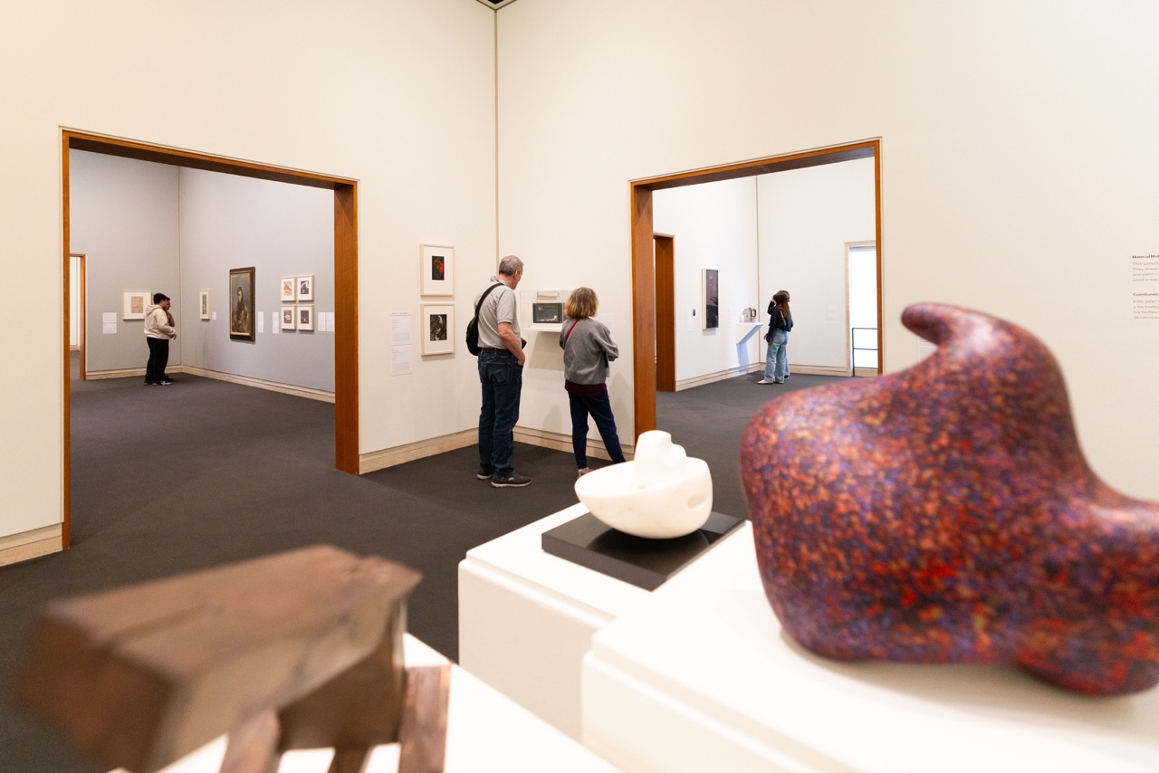 Gallery interior with sculptures and framed artworks; visitors observing displays.